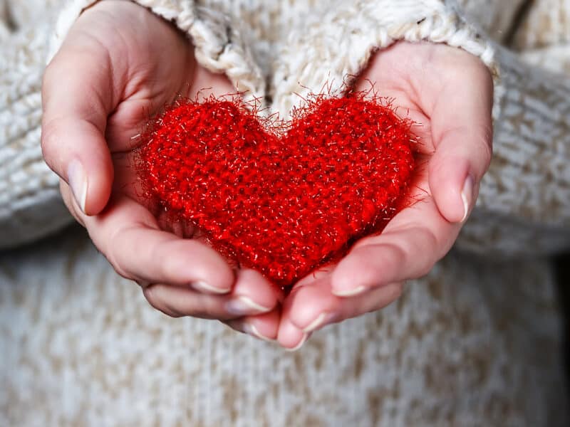 Girl in a light sweater gives a knitted heart. Close-up
