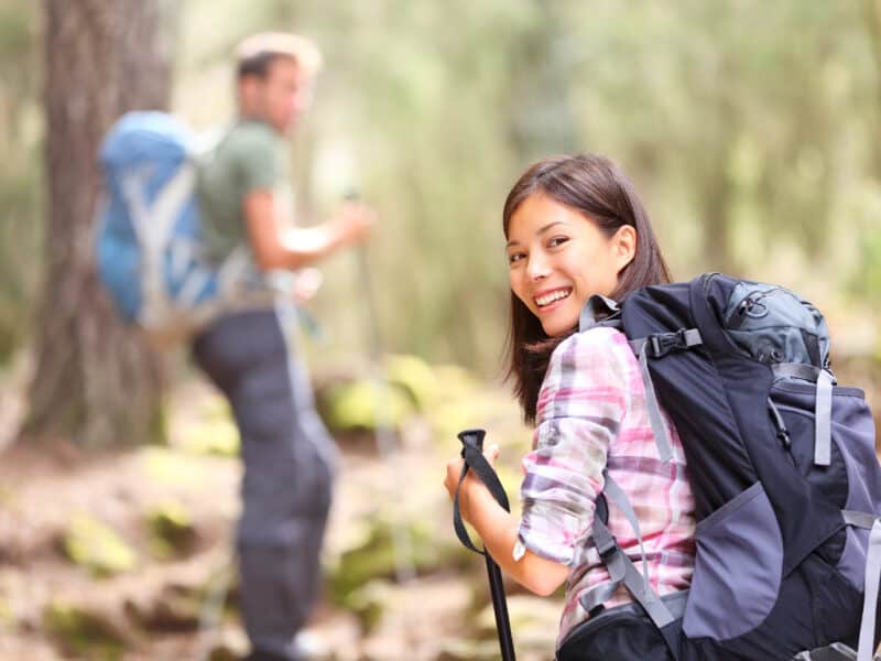 "Hikers. Couple hiking in forest. xwoman hiker smiling happy at camera walking with hiking poles. Young man in background. From Aguamansa, Tenerife, Spain."